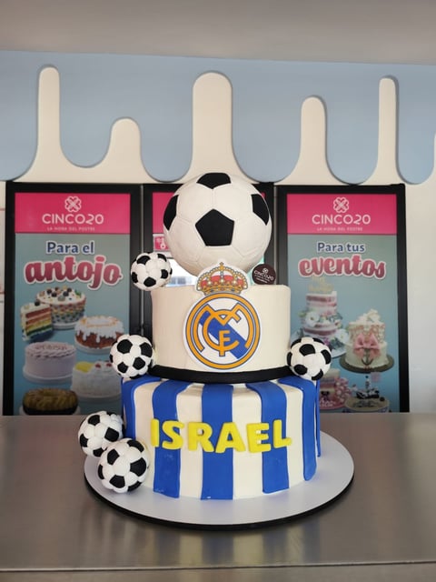 Multi-tiered Real Madrid themed cake with soccer ball decorations, blue and white stripes, and white fondant toppers