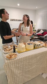 Man and woman chat at a dessert table with pastries and cakes during an indoor gathering