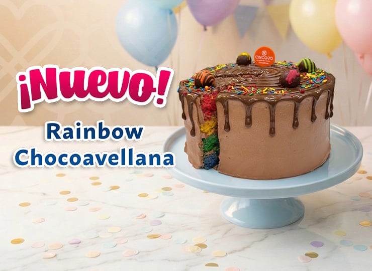 Chocolate cake with rainbow layer and candy decorations on blue pedestal with colorful balloons and Nuevo Rainbow Chocoavellana text
