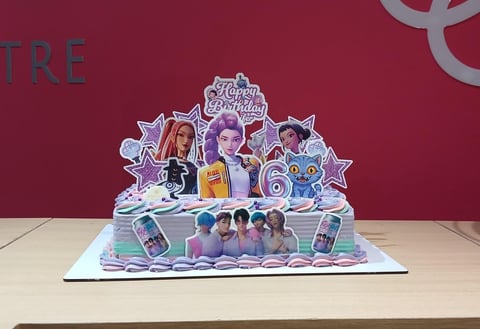 Colorful birthday cake with purple decorations, character cutouts, and number 6 candle on a maroon backdrop