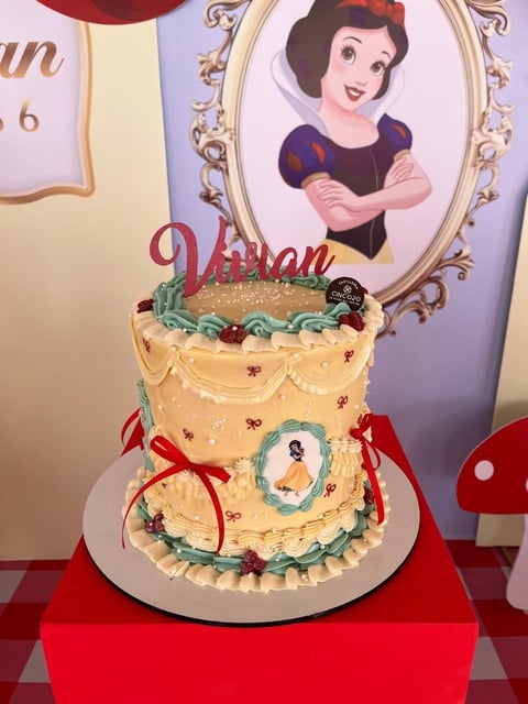 Snow White themed birthday cake with cream frosting, decorative piping, and Snow White cake topper on red display box