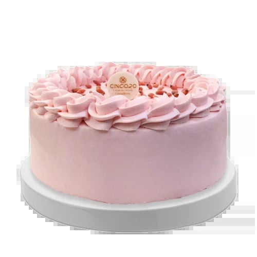 Pink frosted cake with ruffled flower decoration on white plate, featuring a gold ornament on top